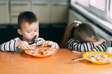 Wall Mural - Boy and girl in the kitchen eating pasta are very hungry, the girl does not like it upset