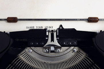 Fototapete - Old retro vintage black typewriter with close-up typing text Share your story as heading on aged paper