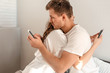 © estradaanton - Young couple in the bedroom. Side view of unfaithful man and woman are cheating on the phone while hugging each other