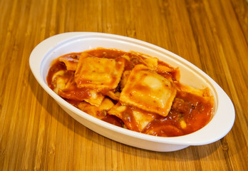 Wall Mural - Fresh cooked ravioli in a tomato sauce in a white dish on a wood cutting board.