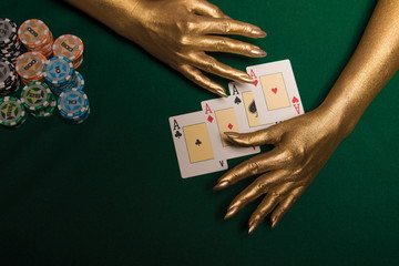 Green card table with cards and chips and gold female hands