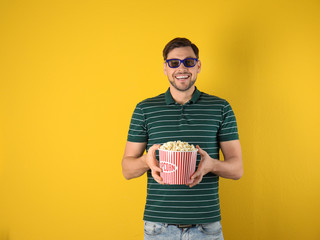 Canvas Print - Man with 3D glasses and tasty popcorn on color background. Space for text