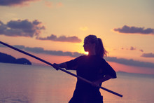 Young Beautiful Girl Woman Blond Doing Kung Fu With Bamboo Stick On The Seashore At Sunset