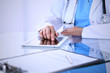 © rogerphoto - Woman doctor using tablet computer while standing straight in hospital office, closeup. Healthcare, insurance and medicine concept