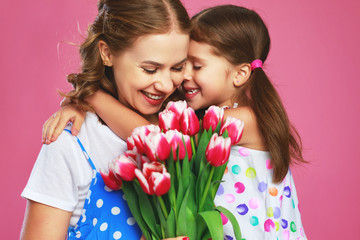 happy mother's day! child daughter   gives mother a bouquet of flowers on color pink background.