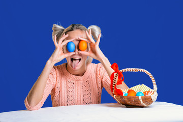 Wall Mural - A cheerful young girl closed her eyes with Easter eggs and stuck out her tongue on a colored background.