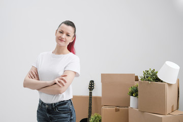 Wall Mural - Young beautiful girl with colored hair in a white T-shirt and jeans, against the background of cardboard boxes and things.