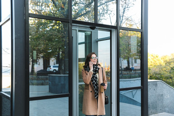 Wall Mural - Woman outdoors walking by street drinking coffee talking by mobile phone.