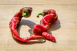 Two curvy cayenne peppers on a wooden block next to each other
