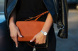 Luxurious young woman in black leather jacket holding orange purse