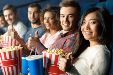 Cinema fans all here. Group of cheerful friends showing thumbs up together sitting in the movie theatre