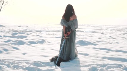 Wall Mural - cute brunette walks along snowy field, a girl with long dark hair has her back to the camera, no face on video, lady in vintage gray adorable light dress pulls royal weapon of snow behind her