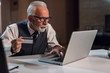 © Drazen - Senior businessman using laptop and making payments online with a credit card.
