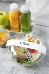 Container with delicious food and bottles of juice on table