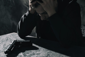 Wall Mural - Depressed young man with gun at table. Suicide awareness concept