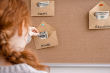 Woman Putting Money In Envelopes For Different Needs. Concept Of Savings