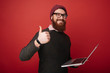 © Vulp - Everything works great. Delighted joyful bearded man holding his laptop while showing a thumbs up gesture