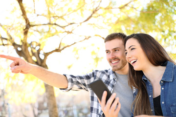 Wall Mural - Happy couple holding phone pointing location in a park