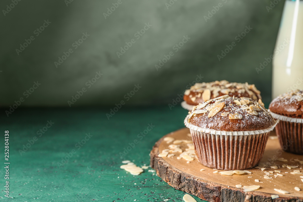 Board with tasty almond muffins on color table