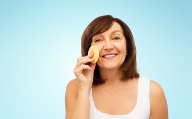 Sticker - beauty, skin care and old people concept - smiling senior woman cleaning her face with exfoliating sponge over blue background