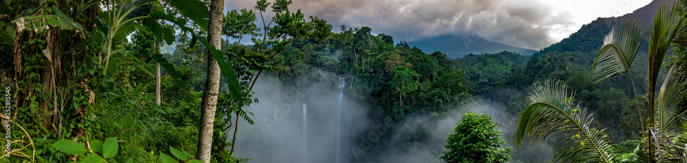 Aerial over Sekumpul waterfall surrounded by dense rainforest and mountains shrouded in mist at sunrise, Bali, Indonesia panoramic - obrazy, fototapety, plakaty 