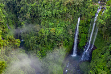 Fototapete - Aerial over Sekumpul waterfall surrounded by dense rainforest and mountains shrouded in mist at sunrise, Bali, Indonesia