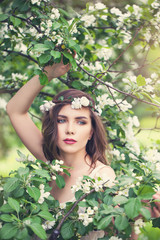 Spring girl face. Pretty young model woman in spring flowers wreath on floral background outdoor