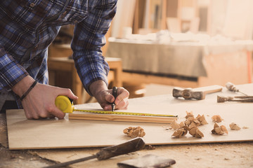 Carpenter working with meter or rule taking measures on wood using pencil. Workshop background