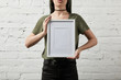 cropped view of woman standing and holding blank white frame in hands