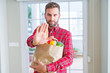 © Krakenimages.com - Handsome man holding groceries bag with open hand doing stop sign with serious and confident expression, defense gesture