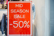 Mid season sale -50% sign in shop window on the red background