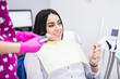 © F8  \ Suport Ukraine - Beautiful young female patient with perfect white teeth sitting in dental chair, looking in the mirror and checking up teeth after treatment at modern dental clinic. Dentistry and healthcare concept