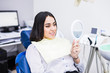 © F8  \ Suport Ukraine - The girl smiles in dentistry. Patient dentist racing woman at the Dental Clinic. White well-groomed teeth after taking a doctor. Tooth whitening and tooth enamel. In the hands of the mirror