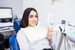 © F8  \ Suport Ukraine - The girl smiles in dentistry. Patient dentist racing woman at the Dental Clinic. White well-groomed teeth after taking a doctor. Tooth whitening and tooth enamel. In the hands of the mirror