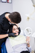 © F8  \ Suport Ukraine - Young woman is sitting in a dental office in a dental chair holding a mirror in front of her are dentists. Happy patient and dentist concept.