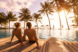 Couple enjoying beach vacation holidays at tropical resort with swimming pool and coconut palm trees near the coast with beautiful landscape at sunset, honeymoon destination