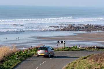 Widemouth Bay, Cornwall, England, UK. February 2019. Widemouth Bay, close to Bude, north Cornwall with a backdrop of the sea at low tide. Small car on the coastal road