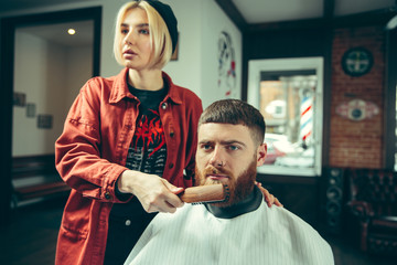 Wall Mural - Client during beard shaving in barbershop. Female barber at salon. Gender equality. Woman in the male profession.