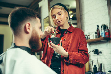 Wall Mural - Client during beard shaving in barbershop. Female barber at salon. Gender equality. Woman in the male profession.