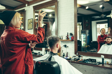 Wall Mural - Client during beard shaving in barbershop. Female barber at salon. Gender equality. Woman in the male profession.