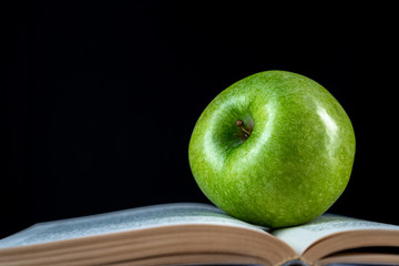 Open book and a green apple in front of black background