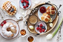Easter Festive Dessert Table With Hot Cross Buns, Cake And Waffles On Linen Table Cloth. Overhead View