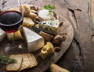 Wall Mural - Cheese platter with organic cheeses, fruits, nuts and wine on wooden background. Tasty cheese starter.