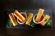 Fried spring rolls on black slate decorated with greens.