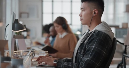 young asian man software developer using computer designing mobile application reading notes brainstorming design solution in modern office workplace