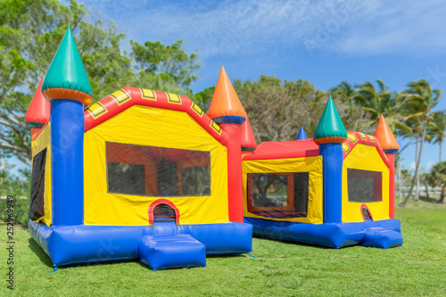 Two multi-color castle bounce houses are ready for the kids. A beautiful sunny is the perfect time to set up bounce houses at the local park.