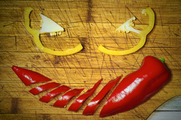 Colorful peppers on rustic wooden table, top view smiley from sliced red and yellow sweet pepper, angry vegan