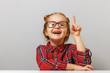 © Olga - Back to school. Funny little girl with glasses points finger up. Education concept. Gray background