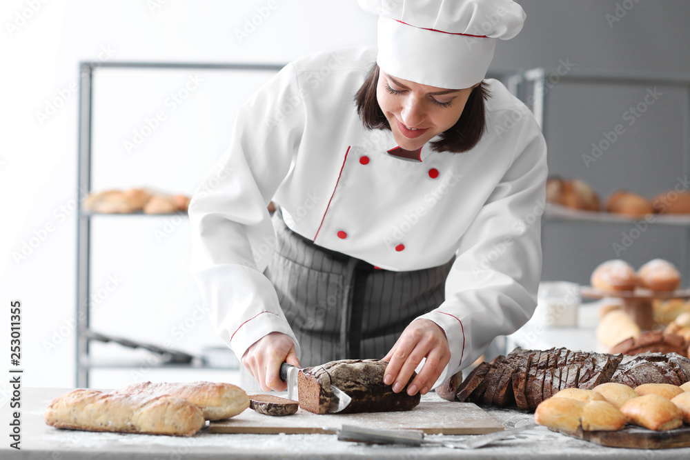 Female baker cutting fresh bread in kitchen