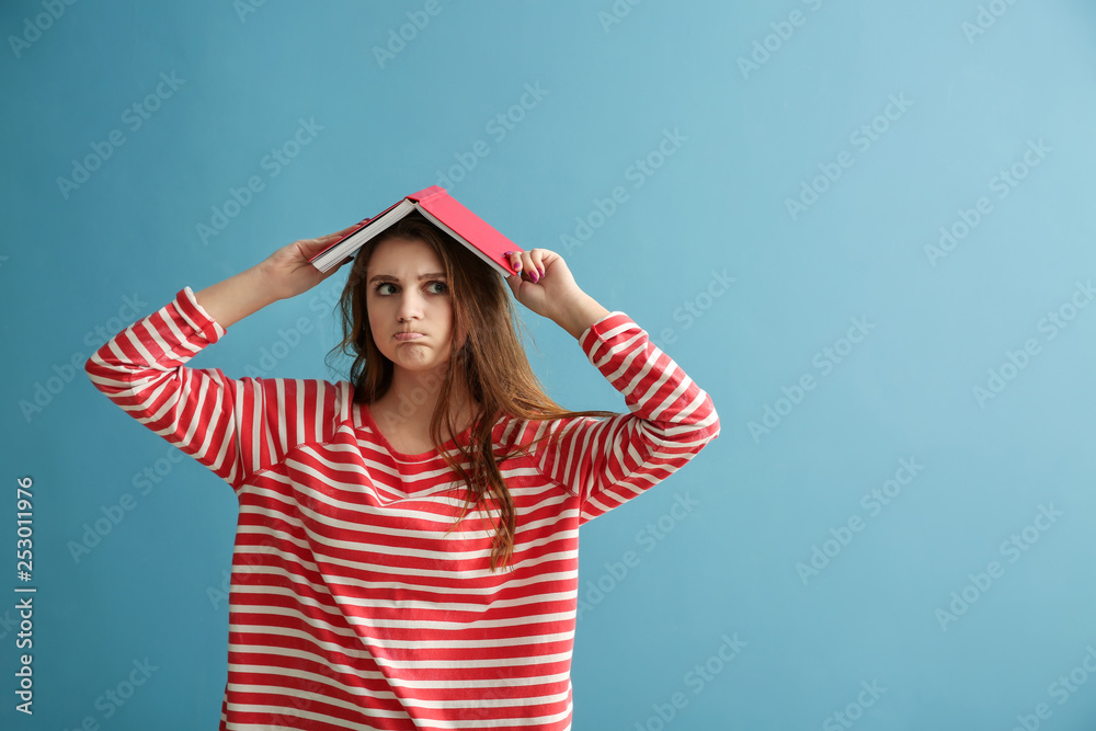 Emotional schoolgirl with book on color background